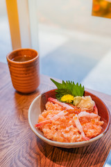 Japanese food, a bowl of minced salmon and shrimp rice and a cup of green tea beside placed on wooden table