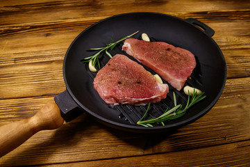 Raw pork steaks ready for preparation with rosemary, garlic and spices in cast iron grill frying...