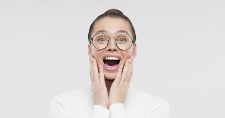 Close up portrait of young woman with wow expression. Pleasantly surprised smiling girl with bugged eyes, holding hands on cheeks with widely open mouth in amazement