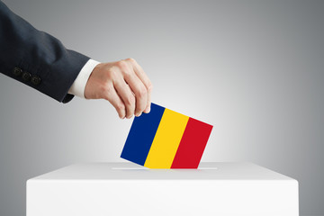 Man putting a voting ballot into a box with Romanian flag.