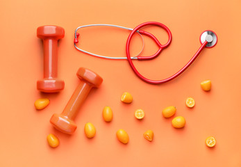 Stethoscope, fruit and dumbbells on color background