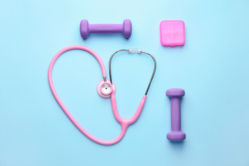 Stethoscope and dumbbells on color background