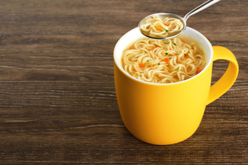 Hot cup of instant chicken noodle soup on wooden background.