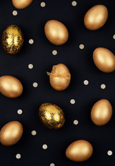 Top view of golden colored Easter eggs decorated with bow and confetti on dark black background. Happy Easter greeting card. Easter background.