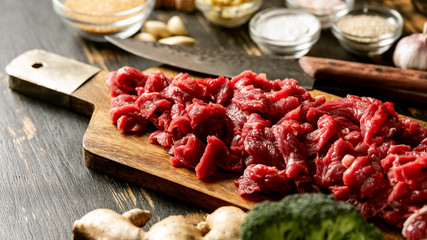 Sliced raw meat for cooking healthy eating recipe with vegetables, spices, sauce and other ingredient on table background.