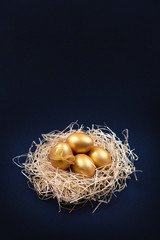 Golden colored Easter eggs in decorative nest on dark blue background. Happy Easter greeting card. Easter background. Place for text.
