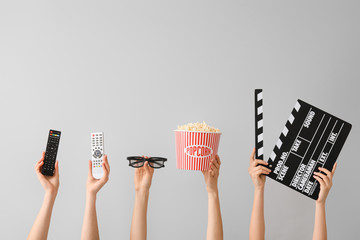 Many hands with popcorn, remote controls, movie clapper and eyeglasses on grey background