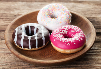 three various glazed doughnuts in plate on wooden background