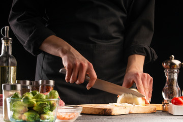 Chef cuts onions for cooking. On a black background. Cooking and Recipe Book. Delicious and wholesome food.