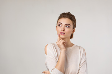Portrait of cute brunette woman thinking about something on gray background. Human emotions, facial...