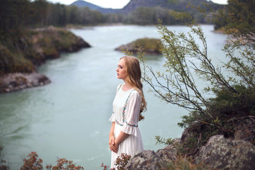  A girl in a white dress walks on a rocky shore near the river.