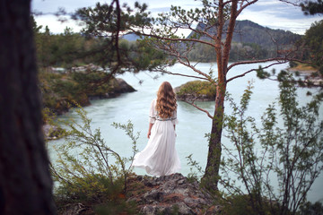  A girl in a white dress walks on a rocky shore near the river.