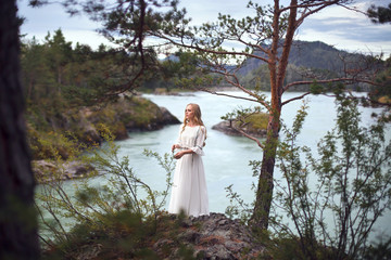  A girl in a white dress walks on a rocky shore near the river.