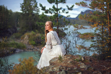  A girl in a white dress walks on a rocky shore near the river.