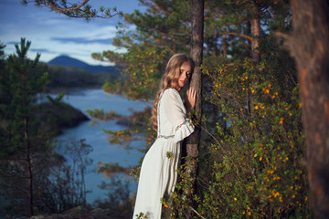  A girl in a white dress walks on a rocky shore near the river.