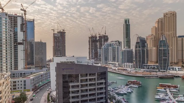 Yachts in Dubai Marina flanked by the Al Rahim Mosque and residential towers and skyscrapers aerial timelapse. Modern high rise skyline with boats and wooden dhows