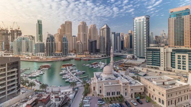 Yachts in Dubai Marina flanked by the Al Rahim Mosque and residential towers and skyscrapers aerial timelapse. Modern high rise skyline with boats and wooden dhows