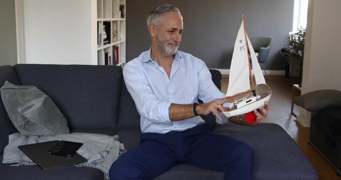 Man sitting on a couch and viewing a sailing boat model