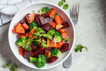 Baked sweet potato, beetroot and broccoli salad in white bowl, top view.