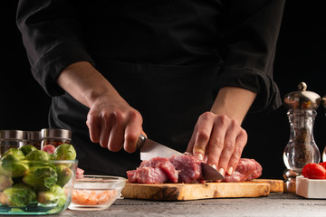 Cooking, the chef cuts pork meat on a background of vegetables. Cooking. Recipe book, cooking and gastronomy