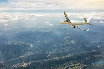 Airplane flying at high altitude over green mountains and sky at sunrise