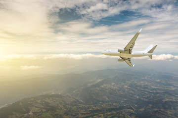 Airplane flying at high altitude over green mountains and sky at sunrise