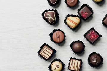 Top view of various chocolate pralines on wooden background