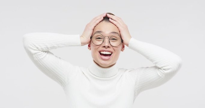 Surprised young girl in white sweater and round glasses shouting oh my god wow with open mouth, shocked by low price and sales, isolated on studio gray background