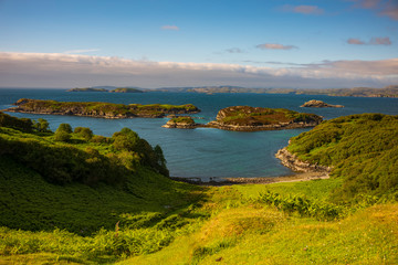 The view of islands and a rocky beach from top of a hill named Drumbeg Viewpoint, is soaked in daylight duing a summer day, along the North Coast 500 route in Scotland. 