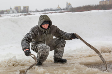 Slinger in protective workwear with a hood on his head, slings under the ice block