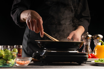 Chef cook fried in a pan against the background of fresh vegetables, culinary recipes