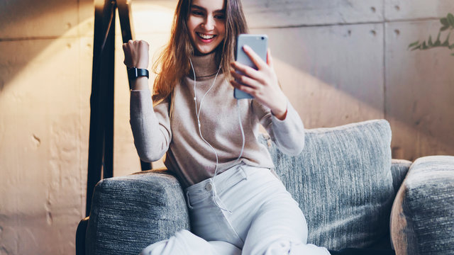 Girl taking photo of herself on camera of mobile phone. Young woman sitting in armchair and making video calls in messenger apps. Shooting stories and selfies, sharing and streaming