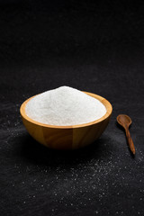 Wooden bowl with sugar on a dark background.