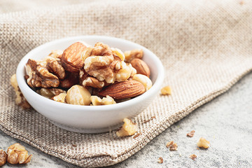 Mixed nuts in white clean bowl on sack cloth. Healthy food and snack concept.