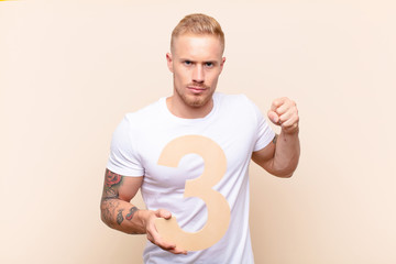young blonde man angry, anger, disagreement, holding a number 3.