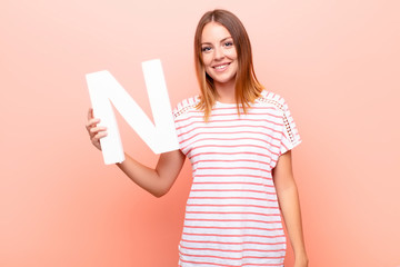 young pretty red head woman excited, happy, joyful, holding the letter N of the alphabet to form a...