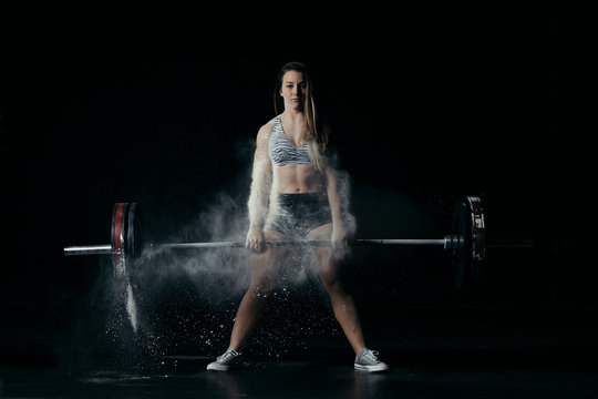 Strong woman making a workout with a bar on black background and white explosion on her back