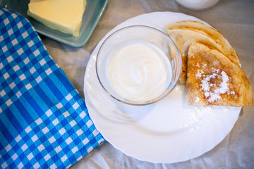 Pancakes on a white plate with powdered sugar and sour cream