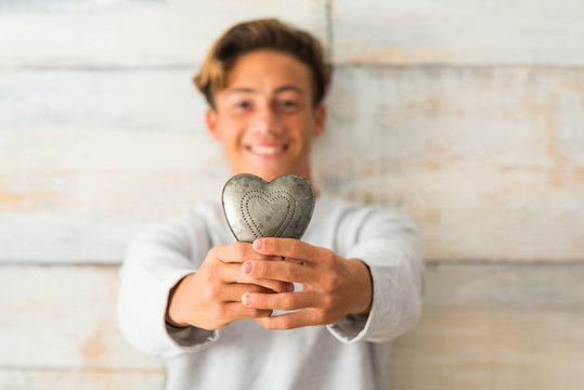 close up of teennager holding an metal heart at home with a wooden background - oy giving his heart concpet