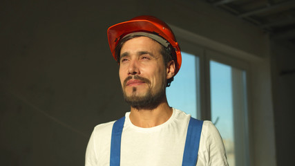 Slow motion, smiling builder stands and puts on protective helmet