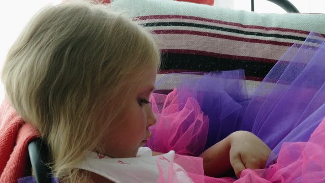 Little girl ballerina is sad at the window. Baby misses home alone