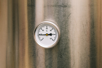 An industrial thermometer is mounted on a stainless steel boiler. Heated cold water. Temperature...
