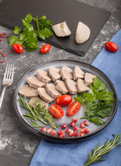 Boiled pork tongue with tomatoes and herbs on a black concrete background. side view, close up.