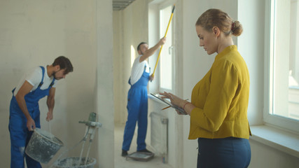 Woman stands with tablet and watches how builders work 