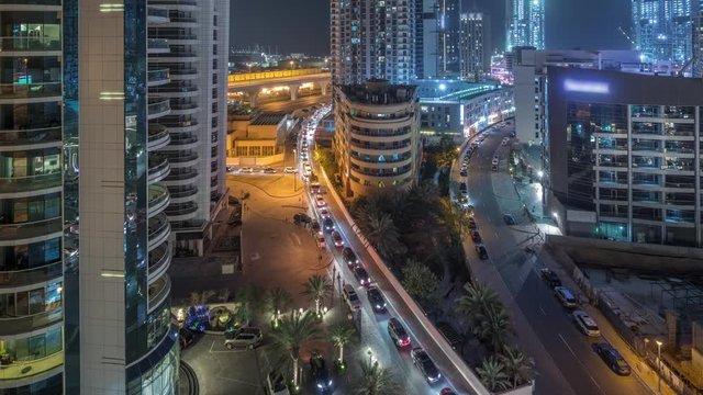 Dubai Marina with illuminated skyscrapers and promenade aerial night timelapse. Modern towers and boats from above with traffic on a road. United Arab Emirates