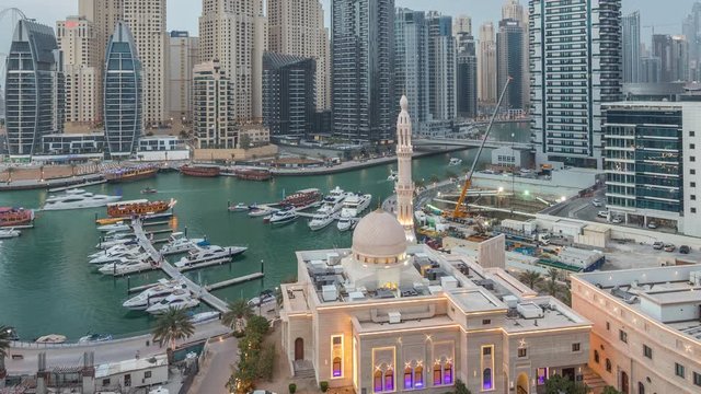 Yachts in Dubai Marina flanked by the Al Rahim Mosque and residential towers and skyscrapers aerial day to night transition timelapse. Modern high rise skyline with boats and wooden dhows