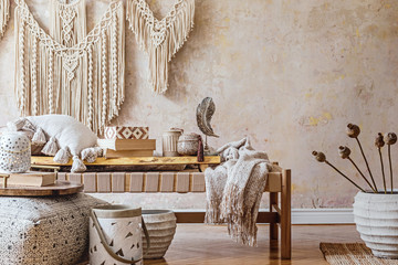 Stylish oriental living room with design beige chaise longue, beautiful macrame, pouf, pillows, white pot with flowers and elegant personal accessories. Wabi sabi concept. Grunge wall. Home decor.