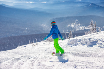 Snowboarder in background of ski resort, back view, high mountains, sunny day