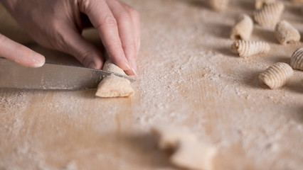 Fototapeta na wymiar Close up process of homemade vegan gnocchi pasta with wholemeal flour making. The home cook cuts the dough on the wooden chopping board , traditional Italian pasta, woman cooks food in the kitchen