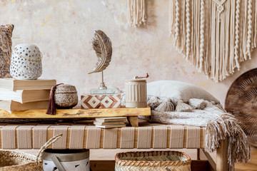 Stylish oriental living room with design beige chaise longue, beautiful macrame, pillows, wooden tray and elegant personal accessories. Wabi sabi concept. Grunge wall. Home decor. Template.